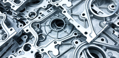 Close-up of numerous machined aluminum parts with circular and angular cut-outs, stacked in a layered pile, highlighting their smooth, metallic finish.