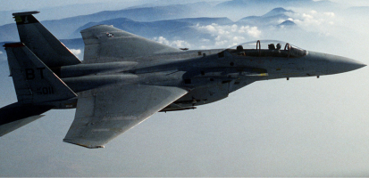 Military fighter jet flying above cloud layer with mountains in the distance, showcasing high-performance aviation equipment.